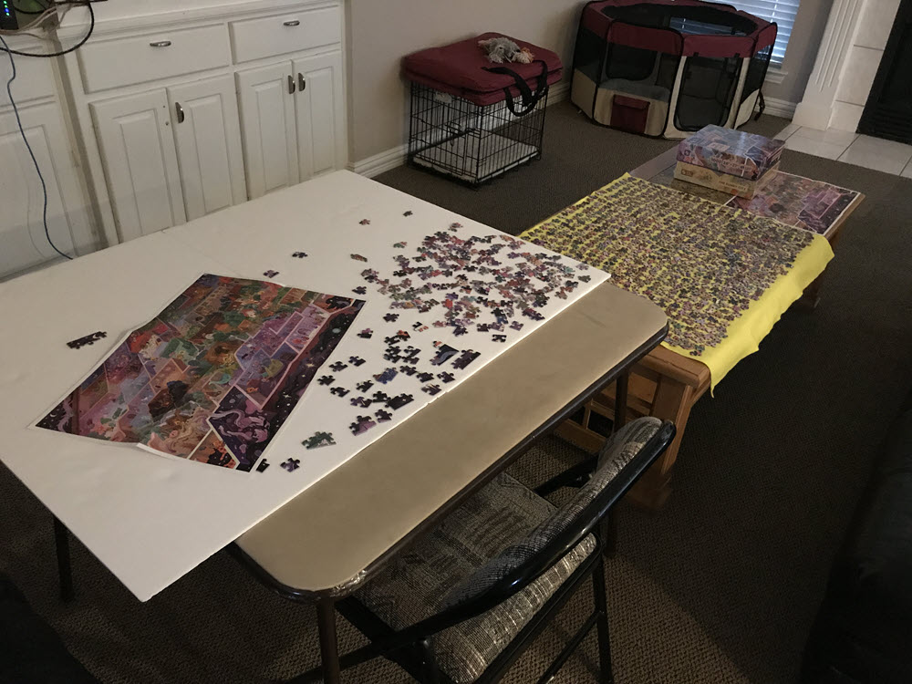 Card table with jigsaw puzzle pieces next to a coffee table covered with puzzle pieces. Automatic ALT text suggested "Indoor."